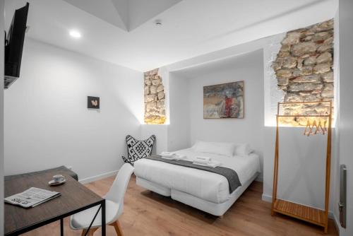 a white bedroom with a bed and a table at 32 De Agosto ROOMS in San Sebastián