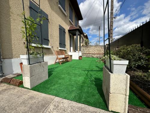 un patio con césped verde y dos macetas en Guest Room avec SDB privée près de Paris, Roissy CDG et du village Olympique, en Persan