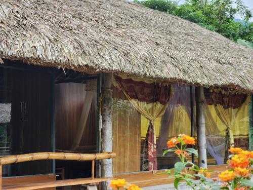 a hut with a thatched roof and flowers at Dong Que Homestay-Tours-Motorbike, Car rental, Hiking in Ha Giang