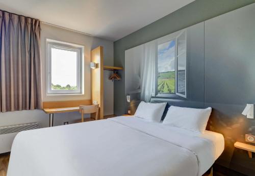 a bedroom with a large white bed and two windows at B&B HOTEL Beaune Sud 2 in Beaune