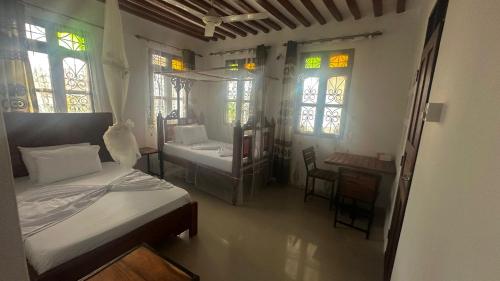 a bedroom with two beds and a table and windows at Light of Zanzibar Hotel in Nungwi