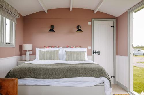 - une chambre avec un grand lit aux murs roses dans l'établissement Barley Shepherd Hut - Snettisham Meadows, à King's Lynn