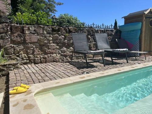 two chairs sitting next to a stone wall next to a swimming pool at Gîte Trotthus maison familiale avec piscine in Hunawihr