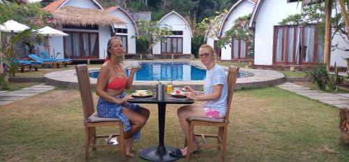 two women sitting at a table in front of a pool at THE OWN PENIDA COTTAGE & SPA in Nusa Penida