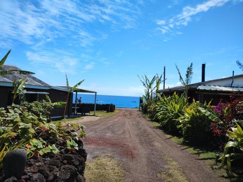 un chemin de terre menant à une maison avec l'océan en arrière-plan dans l'établissement Cabañas Kitai, à Hanga Roa