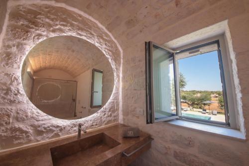 baño con espejo redondo y lavabo en Trulli & Dimore - Trulli Lorusso, en Castellana Grotte