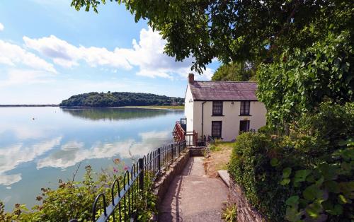 a house on the shore of a body of water at Drefach - Refurbished farmhouse in stunning surroundings with hot tub in Llanwinio