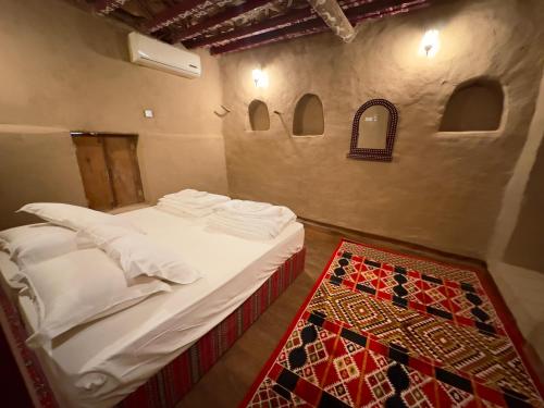 a bedroom with a bed with white sheets and a rug at AL Hamra Heritage Inn in Al Ḩamrāʼ