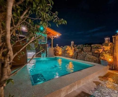 Siargao Vibes Private Resort في Bago: مسبح في الليل بحائط حجري