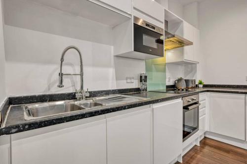 cocina blanca con fregadero y microondas en Heathrow 2-Bedroom Urban Oasis en Londres