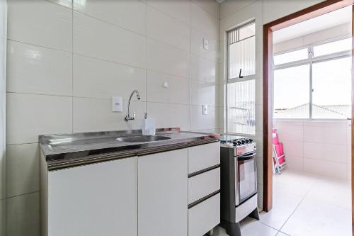 a white kitchen with a sink and a stove at Apto em condomínio pé na areia, c/ piscina MHR308 in Florianópolis