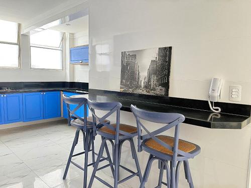 eine Küche mit blauen Schränken und 3 Hockern in der Unterkunft Moderno Vista Mar - AR | Piscina | Vaga Garagem in São Vicente
