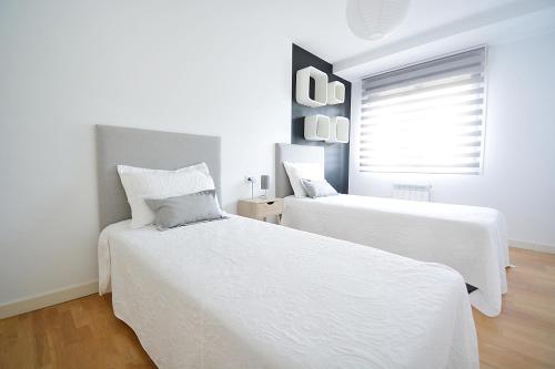two white beds in a white room with a window at GALIHOST - Piso con parking en pleno centro de Cambados in Cambados