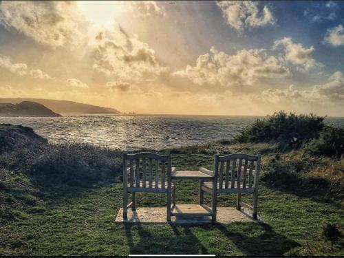 two benches sitting next to a table in front of the ocean at CHINE COTTAGE self-catering coastal bungalow in rural West Wight in Freshwater