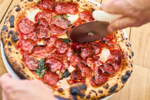 a person cutting a pepperoni pizza with a pizza cutter at Silver Sands Motel & Beach Bungalows in Greenport