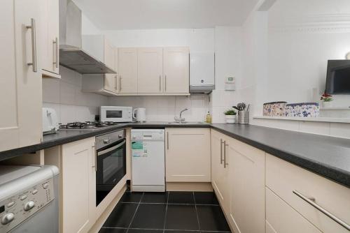 a kitchen with white cabinets and a black counter top at Knightsbridge Two Bed Apartment in London