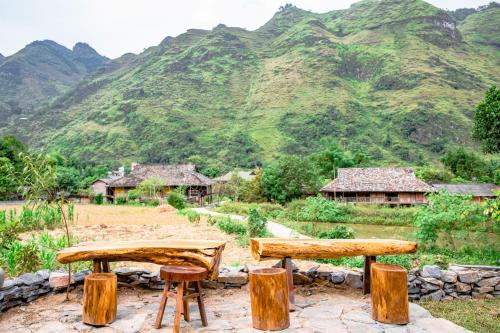 two benches and a table with mountains in the background at Chien's Lodge Du Gia in Làng Cac