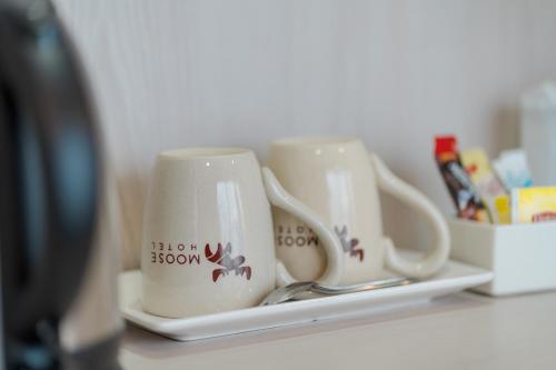 two coffee mugs sitting on a shelf with spoons at Moose Hotel Chiangmai in Chiang Mai