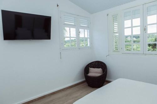 Dieses weiße Zimmer verfügt über einen TV und einen Stuhl. in der Unterkunft Villa F4 chic avec jacuzzi en Martinique in Le Lamentin