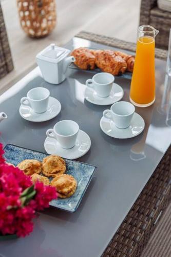 a table with cups and plates of pastries and orange juice at Villa F4 chic avec jacuzzi en Martinique in Le Lamentin