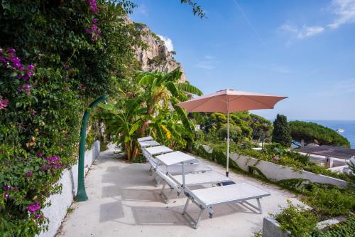 a row of benches with an umbrella and the ocean at Villa Sterlizia in Capri