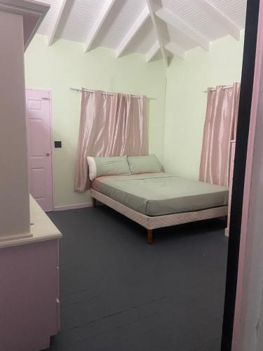 a small bedroom with a bed and pink curtains at Auntie Fiona's Cottage in Vernons