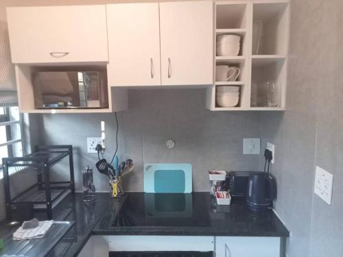 una cocina con encimera negra y armarios blancos en Two bedroom flatlet in Panorama, en Ciudad del Cabo