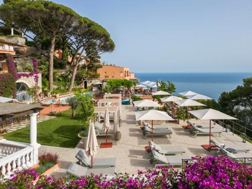 a patio with chairs and umbrellas and the ocean at Hotel Punta Tragara in Capri