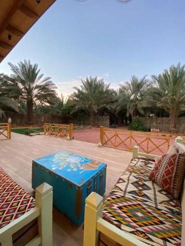 a patio with two beds and a bench and palm trees at كوخ آفيري Aviary Hut in AlUla