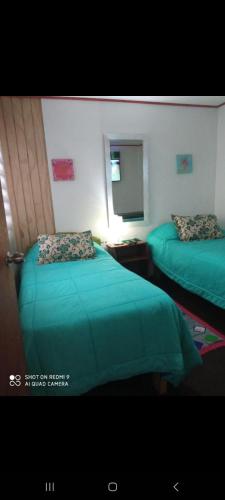 2 camas en una habitación con sábanas verdes y espejo en HOSTAL CHILLAN FAMILIAR, en Chillán