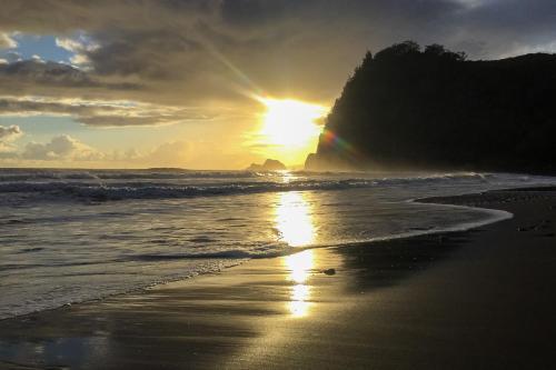 a sunset on the beach with the ocean and a rainbow at A Cozy Cabin In The Country in Hawi
