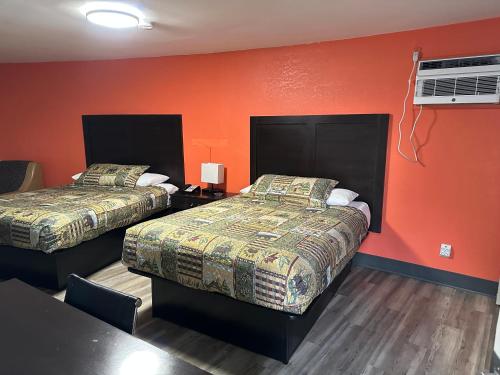 2 camas en una habitación con paredes de color naranja y una mesa en Whispering Pines Motel, en Asheville