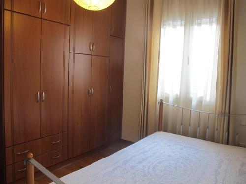 a bedroom with a bed and wooden cabinets and a window at One Home ~ Fits All in Mouzákion