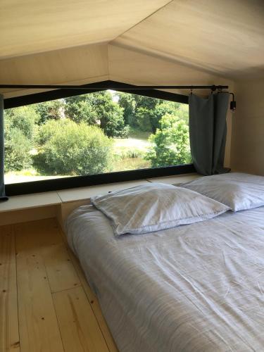 La Tiny House coté pré في Plonéour-Lanvern: سرير في غرفة مع نافذة كبيرة