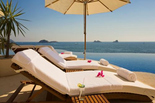 eine Gruppe von Betten mit Sonnenschirm am Strand in der Unterkunft Cala de Mar Resort & Spa Ixtapa in Ixtapa