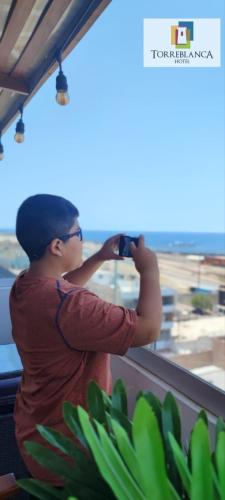a woman taking a picture of the ocean from a window at Torreblanca Hotel in Ilo
