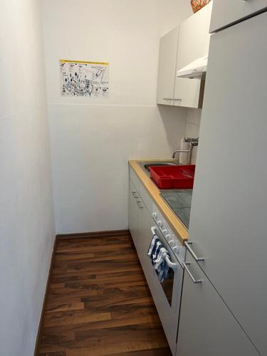 a small kitchen with white cabinets and a red sink at Helle FeWo am Waldrand - mit Balkon, Pool & Sauna in Freyung