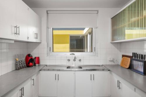 eine weiße Küche mit einem Waschbecken und einem Fenster in der Unterkunft A Larger Slice of Fremantle 3bed apt. Wifi-Netflix in Fremantle
