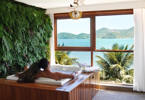 a woman laying in a bath tub in a room with a large window at Catalina Hotel in Ubatuba