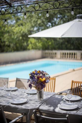 - une table avec un vase de fleurs à côté d'une piscine dans l'établissement Le Mas de la Catounière, à Castillon-du-Gard