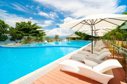 a swimming pool with white chairs and an umbrella at H Resort Bohol - The Coral Cliff by SMS Hospitality in Calape