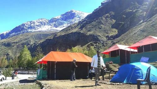 two people standing in front of tents and mountains at Buddy Hikers Stay Badrinath in Badrīnāth