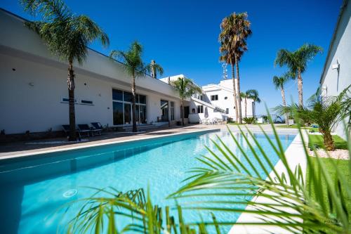 a swimming pool in front of a building with palm trees at New River Hotel in Borgetto