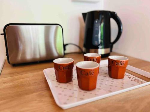 3 tasses à café assises sur un plateau de découpe à côté d'un grille-pain dans l'établissement L'Eden : Apt 4 Prs, clim, parking,300 m des plages, à Antibes
