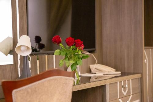 a vase of red roses on a desk with a mirror at Guest House Hotel Apartments in Yanbu