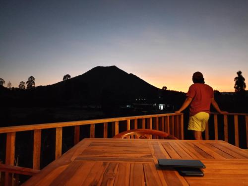 a man standing on a deck watching the sunset at Batur Homestay and Lodge in Bangli