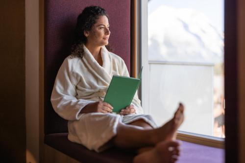 a woman sitting in a bathrobe looking out of a window at Biohotel Leutascherhof in Leutasch