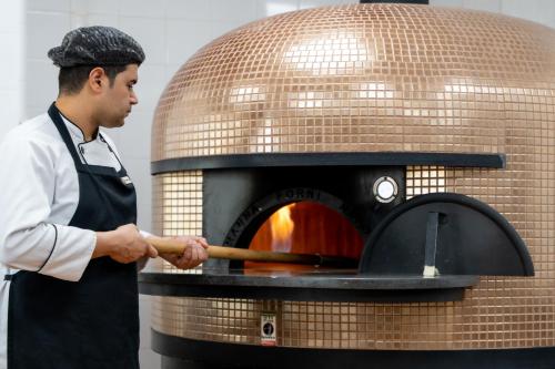 a man in an apron is putting a pizza into an oven at S Plaza Suites Hotel in Seef