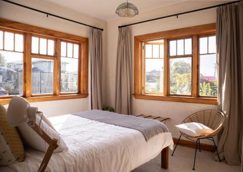 KOWHAI COTTAGE في كايكورا: غرفة نوم بسرير وكرسي ونوافذ