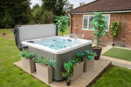 a hot tub in a yard with potted plants at Deluxe 2 Bed Versace Bungalow Hot Tub, Sky TV, Cinema Screen Saffron Walden in Saffron Walden